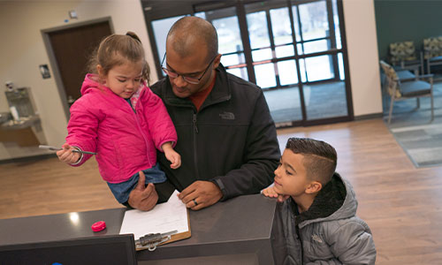Image of father with young daugher and young son signing into the medical clinic.